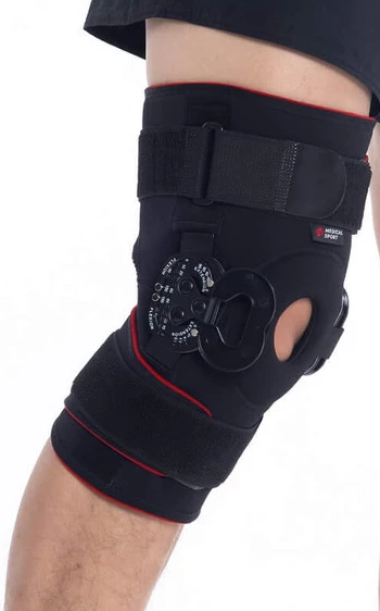 Orteza kolana z mechanizmem rotacyjnym i paskiem, czarna z czerwonymi akcentami, zapewniająca stabilizację i wsparcie.