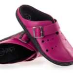 Różowe kapcie z czarną podeszwą, regulowanym paskiem i perforacjami, przeznaczone dla dzieci.