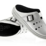 Białe, miękkie buty z czarnym wykończeniem i regulowanym paskiem na rzep, przeznaczone do użytku w domu lub na co dzień.