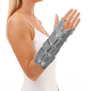 Kobieta z unieruchomioną ręką w gipsowym opatrunku na przedramieniu, uniesiona do góry.