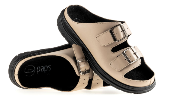 Kapcie na rzepy w kolorze beżowym z czarną podeszwą i wyściółką, otwarte na palce, przeznaczone do użytku domowego.