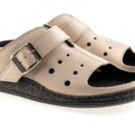 Beżowe kapcie z czarną podeszwą, otwarte z regulowanym paskiem na sprzączkę.