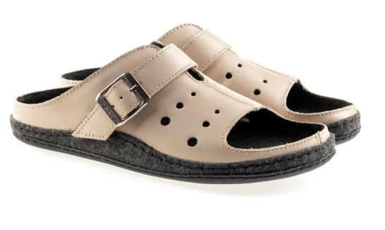 Beżowe kapcie z czarną podeszwą, otwarte z regulowanym paskiem na sprzączkę.