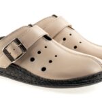 Kapcie z beżowej skóry z regulowanym paskiem i perforacjami, na czarnej podeszwie.