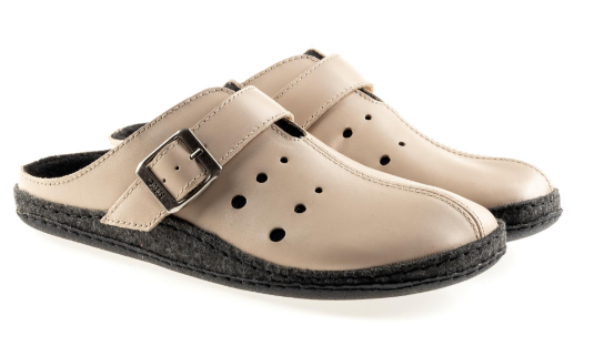 Kapcie z beżowej skóry z regulowanym paskiem i perforacjami, na czarnej podeszwie.