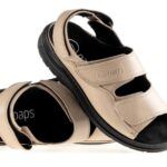 Beżowe sandały na czarnej podeszwie z dwoma szerokimi rzepami, ułożone na boki.