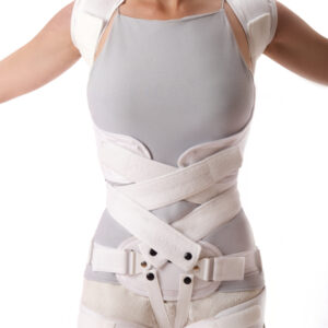 Osoba w specjalistycznym gorsetach ortopedycznych, z widocznymi paskami i zapięciami, na jasnym tle.