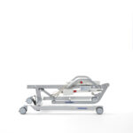 Leżanka medyczna na kółkach, biała, z regulowanym zagłówkiem i podnóżkiem, używana w placówkach zdrowotnych.