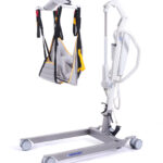 Podnośnik transportowy z uprzężą i mechanizmem podnoszenia, używany do przenoszenia osób o ograniczonej mobilności.