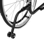 Rama i koła wózka inwalidzkiego z czarnym ramieniem i metalowymi szprychami, widok z boku na podłodze.