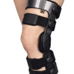 Knee brace z czarnymi paskami i elementami z włókna węglowego, wyposażony w czujniki i regulowane zapięcia.