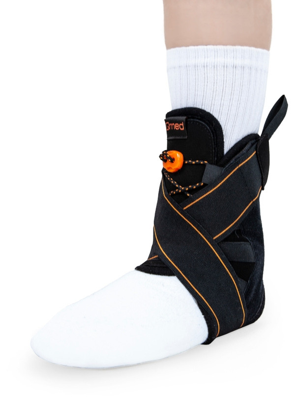 Orteza stopy z czarnym opaskiem, zapięciem na rzep i pomarańczowym elementem, zakładana na stopę w białym skarpecie.