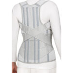 Osoba nosząca ortopedyczny gorset wspierający kręgosłup, widziana od tyłu, w białej odzieży.