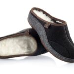 Ciepłe kapcie z czarnego materiału, wyściełane białą wełną, z brązowymi wykończeniami i zapięciem na rzep.