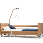 Łóżko szpitalne z drewnianą ramą, poduszkami, pasem bezpieczeństwa i podnośnikiem do podnoszenia pacjentów.
