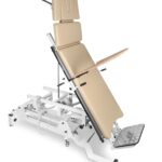 Stół do badania z regulowanym oparciem, podłokietnikami i podnóżkiem, na metalowej ramie z kółkami i mechanizmami regu