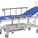 Szpitalny łóżko z niebieskim materacem, barierkami i kółkami, wyposażone w urządzenia do podnoszenia i regulacji pozyc