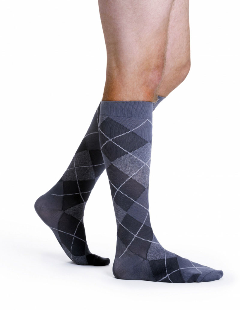 Mężczyzna nosi długie skarpetki w szary i czarny wzór argyle, sięgające do kolan, na białym tle.