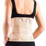 Osoba z założonym ortozą na plecach, widoczna od tyłu, ubrana w czarny top.