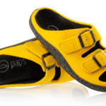 Żółte kapcie z dwoma regulowanymi paskami i czarnymi wstawkami, miękkie, na płaskiej podeszwie.