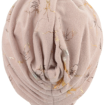 Beżowa czapka z nadrukiem gałęzi i złotymi akcentami, ułożona na białej głowie.