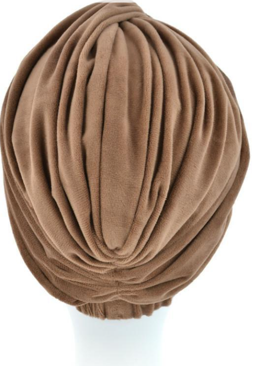 Beżowa czapka z miękkiego, plisowanego materiału, ułożona na białej podstawie.