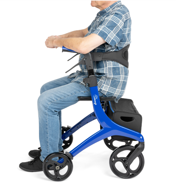 Osoba starsza na specjalnym wózku inwalidzkim z podnóżkiem i torbą pod siedzeniem, ubrana w koszulę i jeansy.