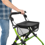 Osoba trzymająca się uchwytu składanej, zielonej laski z koszykiem na zakupy, na białym tle.