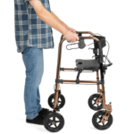 Osoba trzymająca się poręczy lekkiego chodzika z czterema kółkami, ubrana w niebieską koszulę i jeansy.