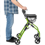 Osoba korzystająca z zielonego chodzika inwalidzkiego z koszykiem, trzymająca uchwyt, na białym tle.