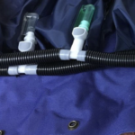 Podłączenie respiratora do maski na niebieskim materiale, z czarnymi rurami i dwoma zaworami.