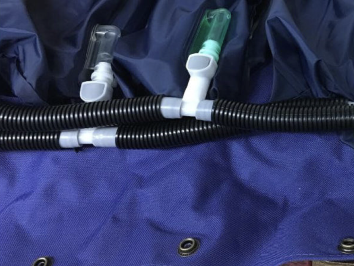 Podłączenie respiratora do maski na niebieskim materiale, z czarnymi rurami i dwoma zaworami.