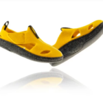 Żółte sandały z czarną podeszwą i otwartymi palcami, uniesione nad powierzchnią, z widocznymi otworami i zapięciem na