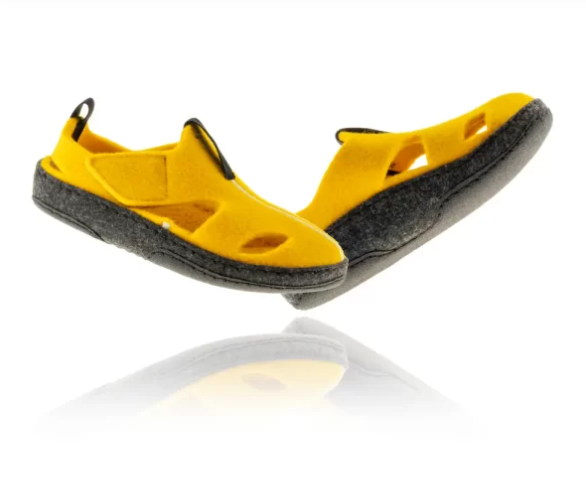 Żółte sandały z czarną podeszwą i otwartymi palcami, uniesione nad powierzchnią, z widocznymi otworami i zapięciem na