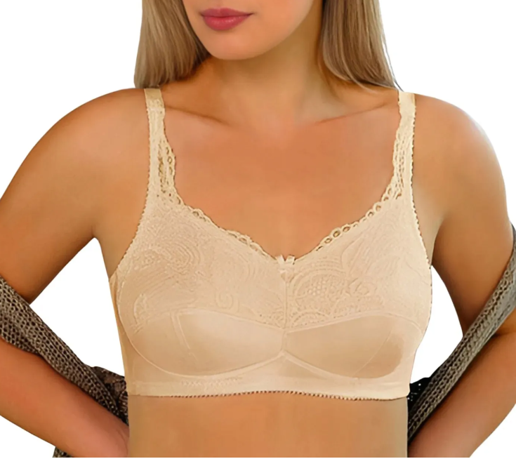 Kobieta w beżowym biustonoszu z koronkowymi ramiączkami, trzymająca się za talię, z częściowo odsłoniętą ramionami.