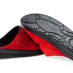 Czerwone kapcie z czarną podeszwą, jedna kapcie leży na drugiej, na białym tle.