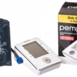 Ciśnieniomierz na nadgarstek, zasilany bateriami, obok opakowania z opisem Złoty Standard i logo marki Pempa.